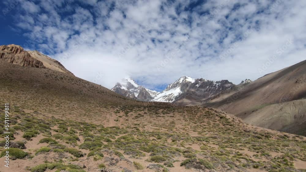 View of the summit of Aconcagua from the approach to basecamp, with blue sky and clouds moving over the mountains creating shadows in the valley View of the summit of Aconcagua from the approach to basecamp, with blue sky and clouds moving over the mountains creating shadows in the valley