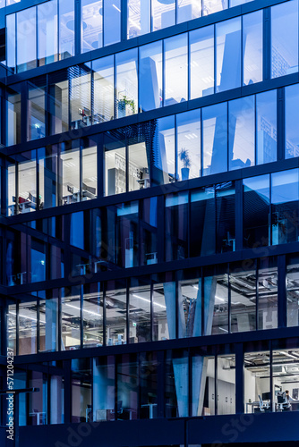 Glass facade of modern multi storey office building at dusk with visible open space offices in oparation and during finishing construction works 