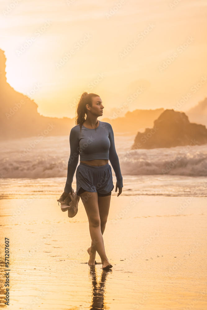 woman walking on the beach with her shoes in her hand while looking at the sea. sunset on the island of tenerife Spain