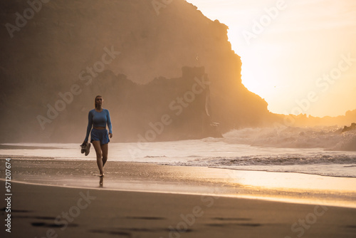 Obraz na płótnie woman walking on the beach with her shoes in her hand while looking at the sea. sunset on the island of tenerife Spain w salonie