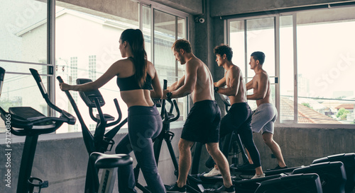 Group of young sporty people doing exercises on elliptical machine at gym. Healthy active lifestyle. Training for muscular body. © winnievinzence