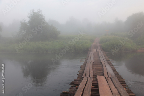 Wooden bridge over the river on a foggy morning.