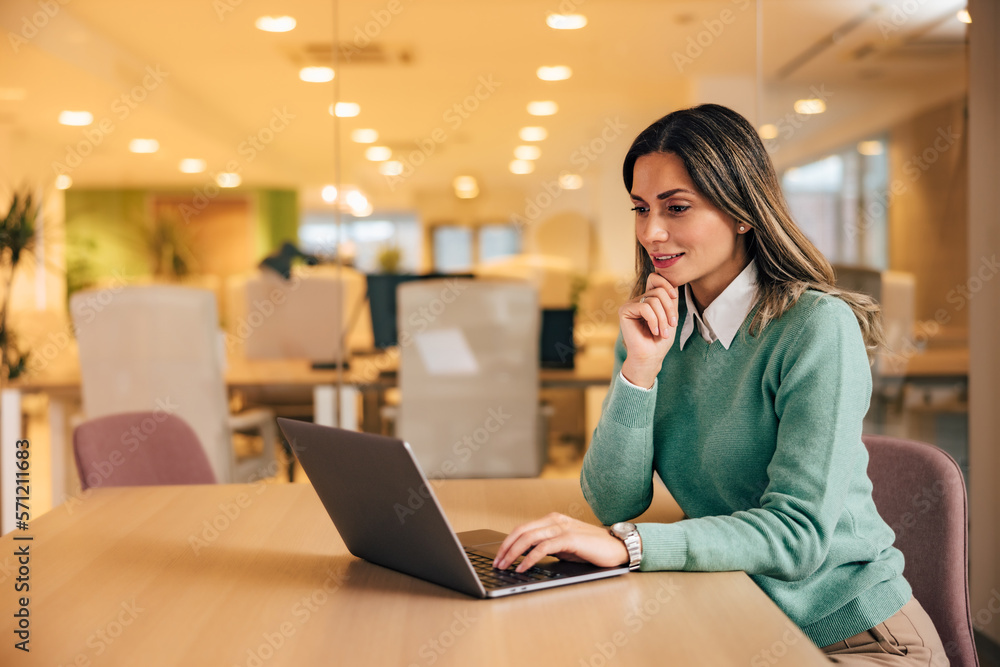 Smiling businesswoman typing on a laptop, sitting at the office, elegantly dressed. Smiling businesswoman typing on a laptop, sitting at the office, elegantly dressed.