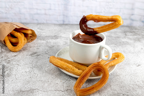 Churro dipping into a cup of hot chocolate on gray stone background, typical Spanish breakfast