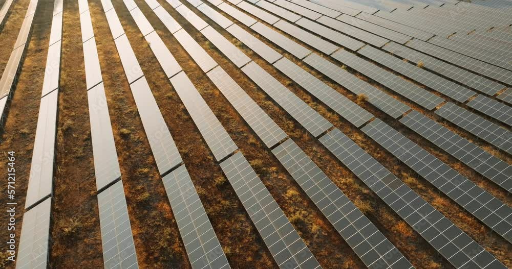 Ecology solar power station panels. Innovation green energy. Alternative energy solar panels aerial view are located on large field near village at sunset in summer slow motion. Ecology solar power station panels. Innovation green energy. Alternative energy solar panels aerial view are located on large field near village at sunset in summer slow motion.