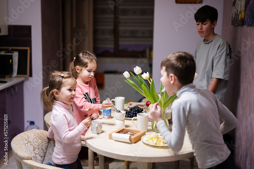 Children eat fruits and desserts  drink tea at home in the evening kitchen.