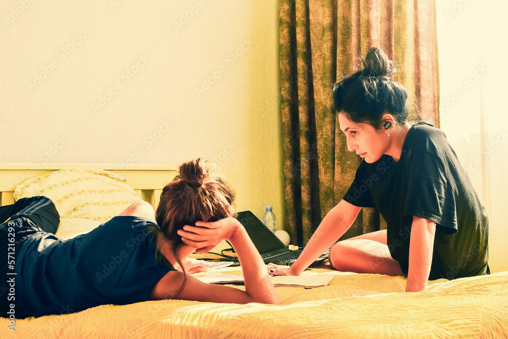 Young mom or babysitter lay on bed and help boy kid with homework