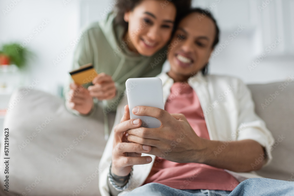 Blurred african american couple using smartphone and credit card during online shopping at home. Blurred african american couple using smartphone and credit card during online shopping at home.