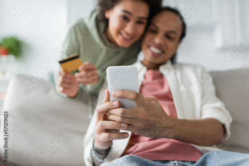Blurred african american couple using smartphone and credit card during online shopping at home.