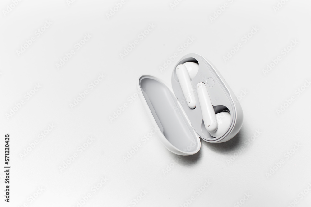 Close-up of modern wireless earbuds lying in charger case on white studio background. Close-up of modern wireless earbuds lying in charger case on white studio background.