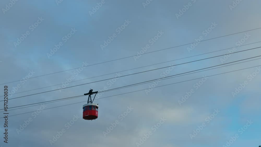 Red cable car on cloudy sky background lift uphill to the Parc de Montjuic station. Entertaining journey for tourists to visit famous Mirador. Gondola transports passengers. Red cable car on cloudy sky background lift uphill to the Parc de Montjuic station. Entertaining journey for tourists to visit famous Mirador. Gondola transports passengers.