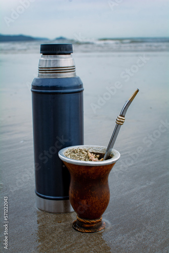 copa de mate de porongo con yerba mate y termo de acero con agua caliente sobre la playa y el agua, disfrutando de una bebida tradicional en la playa. photo