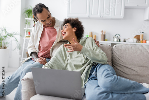 Young african american woman talking to smiling boyfriend near laptop on couch.