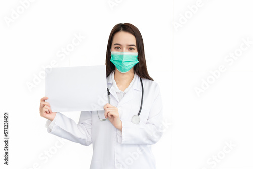 Asian woman professional doctor who wears medical coat and face mask stands and shows white paper to say something isolated on white background in Coronavirus healthcare concept.