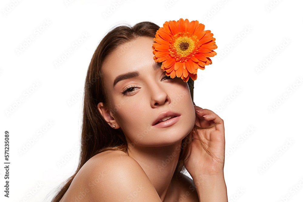 Tender young woman with well-kept skin posing with red gerbera flower over white studio background. Natural ingredients. Concept of natural beauty, youth, health, wellness, femininity