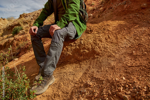man tourist in membrane jacket, tactical pants and hiking boots sits in sand career. Sights of Russia, Siberia and Altai Republic, mars field. Tourism, travel and adventure. Kosh-agach, Chagan-Uzun