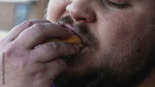 Chubby man eating unhealthy food. Person taking a bite of donut snack