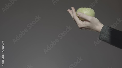 A hand on a dark background holds out a green apple in the palm of your hand. Lending a helping hand.