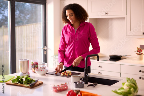 Woman In Kitchen At Home Wearing Fitness Clothing Blending Fresh Ingredients For Healthy Drink