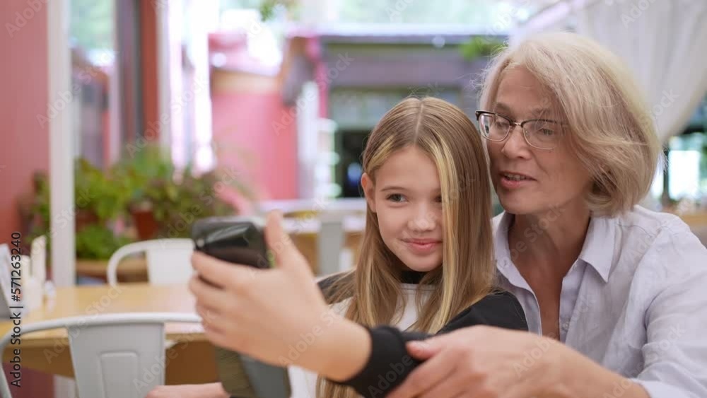 Happy old adult woman granny grandmother and cute adorable small kid child girl granddaughter cuddling having fun together. Look at mobile phone laughing, family love concept, closeup portrait Happy old adult woman granny grandmother and cute adorable small kid child girl granddaughter cuddling having fun together. Look at mobile phone laughing, family love concept, closeup portrait