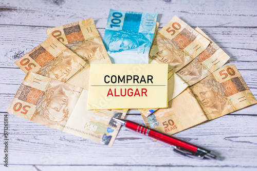 As palavras comprar e alugar em Português do Brasil escrito em um pedaço de papel. Notas do Real Brasileiro sobre uma mesa de madeira na composição. Economia Brasileira e negócios. photo