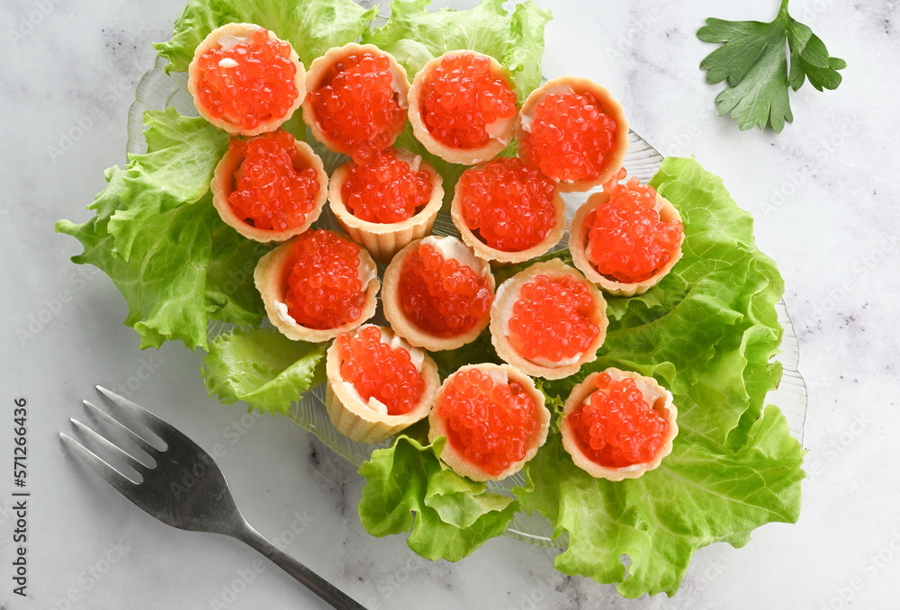 Plate with caviar appetizer decorated with lettuce leaves on a light background