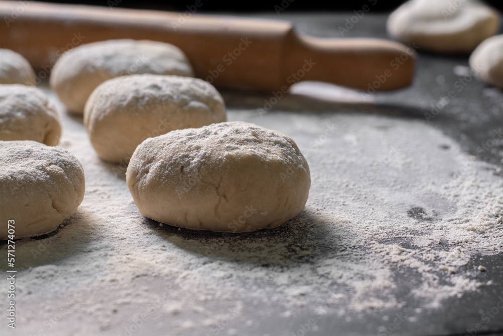 raw bread with rolling pin and scattered flour on black table