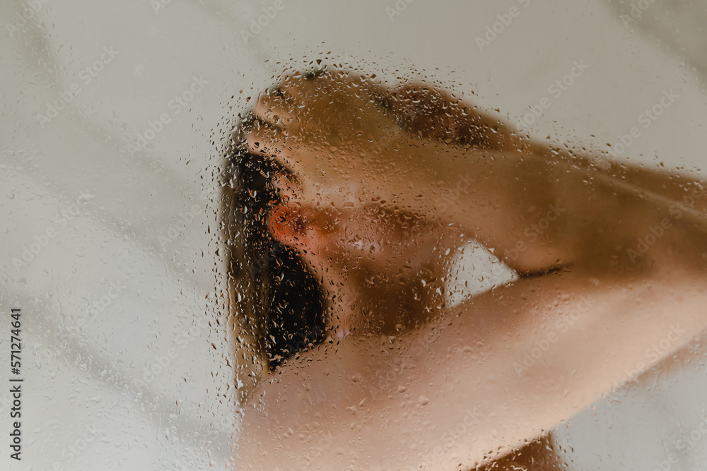 Woman taking shower behind the wet glass. Focus on the droplets. Woman taking shower behind the wet glass. Focus on the droplets.