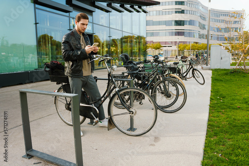 Young man using mobile phone while standing with bicycle outdoors