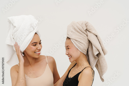 Two beautiful women smiling at each other while posing isolated over white wall