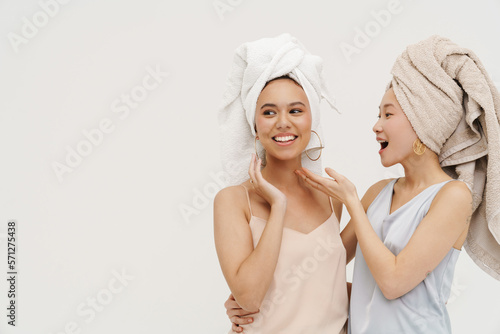 Two beautiful women smiling and gesturing while posing isolated over white wall