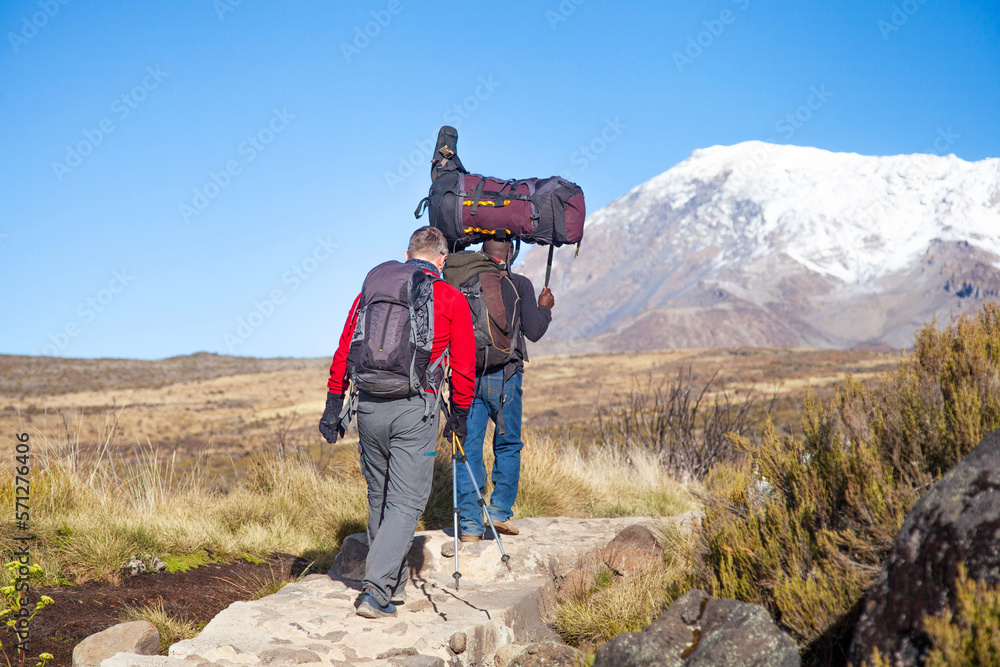 Porters carrying heavy load on his back walks along the road. Porters carrying heavy load on his back walks along the road.