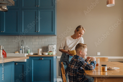 Cute boy eating cookies while sitting in kitchen with mom