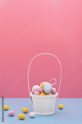 Easter card. Multi Colored sweet chocolate eggs and decorative eggs in white basket on blue and pink background. Copy space for text. Flat Lay
