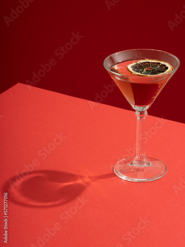 Red cocktail drink in martini glass with dried lemon slice on a red table and red background. Hard light and clean shadow