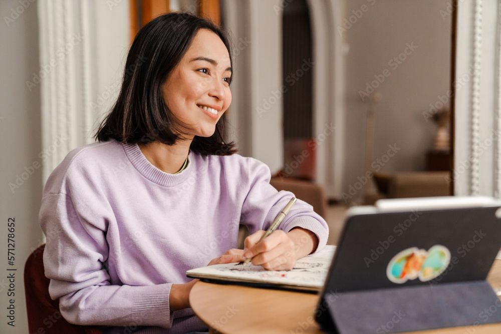 Joyful asian woman drawing while sitting in living room Joyful asian woman drawing while sitting in living room