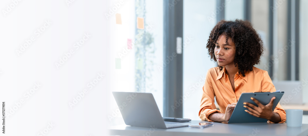 Using laptop computer, Young pretty african american business woman bookkeepers working with balance sheet yearly reports to calculate tax and online consult in modern office. - obrazy, fototapety, plakaty 
