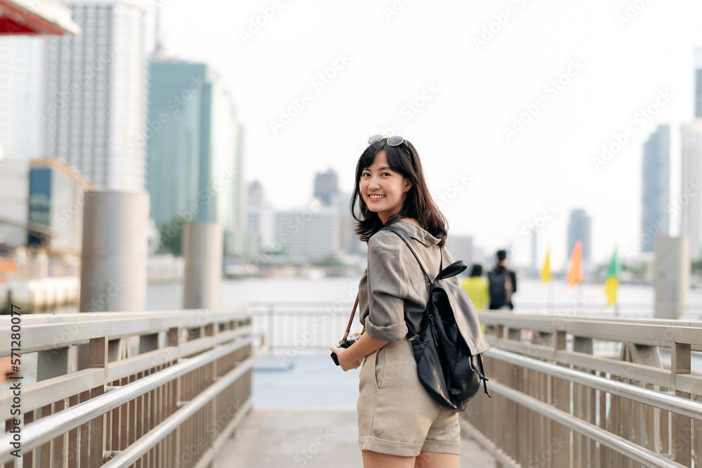 Young Asian woman backpack traveler waiting an express boat at pier on Chao Phraya River in Bangkok. Journey trip lifestyle, world travel explorer or Asia summer tourism concept