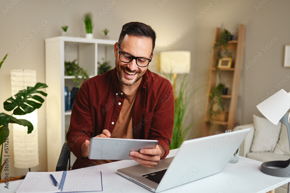 Young man works from home at a desk with a tablet and a laptop Young man works from home at a desk with a tablet and a laptop