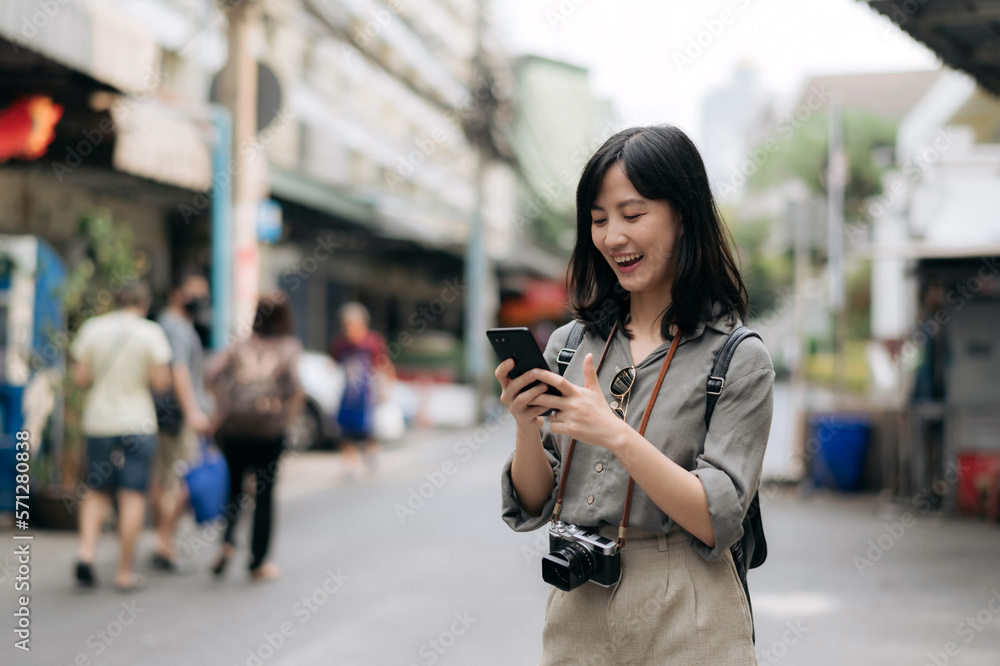 Young Asian woman backpack traveler using mobile phone, enjoying street cultural local place. Traveler checking out side streets. Journey trip lifestyle