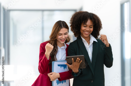 Young trader mixed race woman in formal suit friends consulting and discussing with stock market and cryptocurrency in online trading application. Happy, win, cheerful