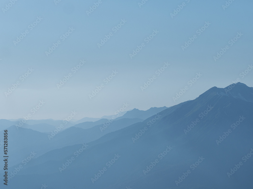 Light blue mountains in the distance, aerial perspective, mountain atmosphere. Beautiful mountain landscape, clouds over the peaks of the mountains,