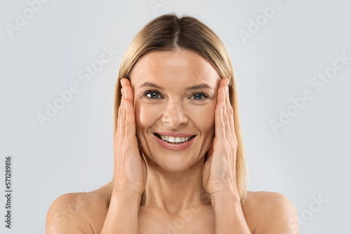 Pretty nude middle aged blonde woman touching face, closeup