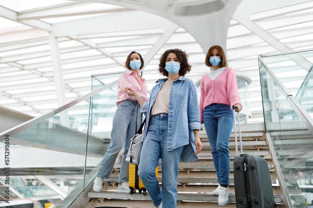 Three Female Friends Wearing Medical Face Masks Posing On Stairs At Airport