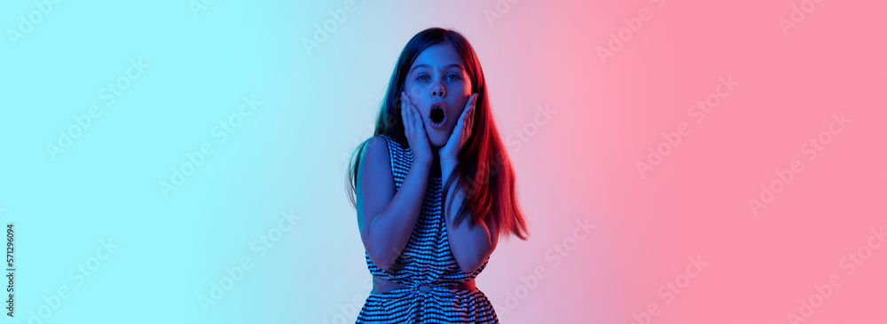 Shocked face. Little girl, child emotionally posing over gradient blue pink studio background in neon light. Concept of childhood, emotions, fun, fashion, lifestyle, facial expression