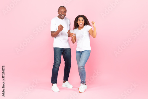 Online lottery. Overjoyed black man and woman rejoicing success and holding smartphone, exclaiming with triumph