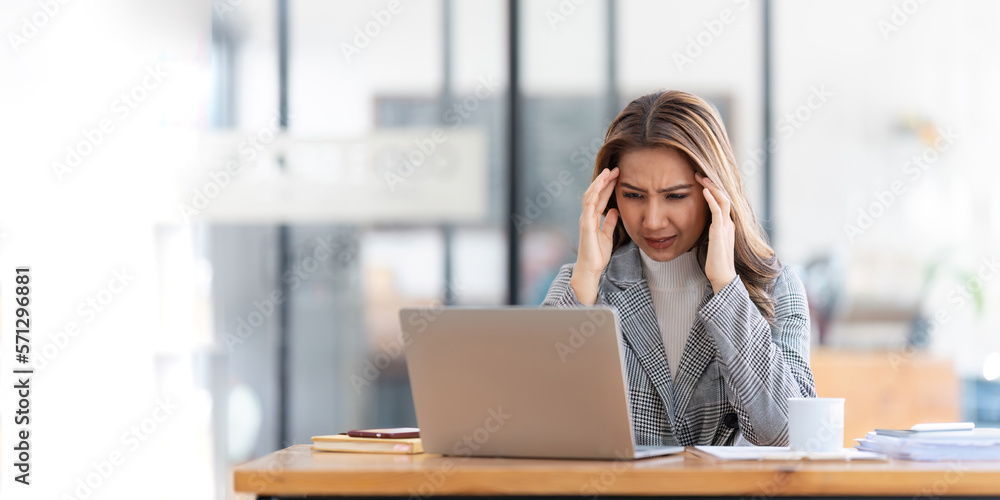 Young businesswoman working on laptop stressed has a headache and thinks hard from work at the office Young businesswoman working on laptop stressed has a headache and thinks hard from work at the office