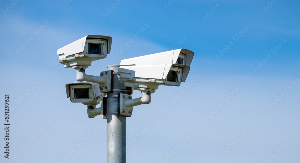 Four security cameras against the blue sky are monitoring. The image has a copy space. Four security cameras against the blue sky are monitoring. The image has a copy space.