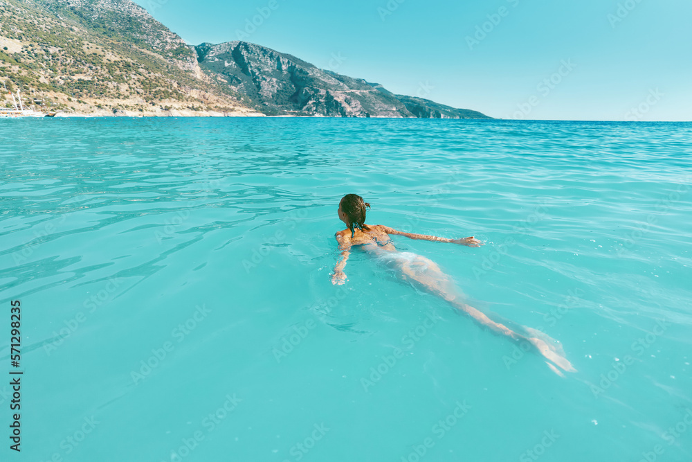 Beautiful paradise vacation woman swimming in the ocean. Carefree girl in bikini floating in transparent turquoise water