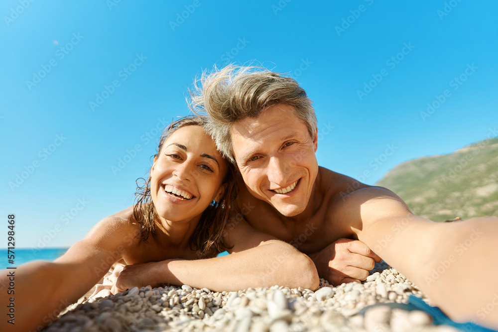 Portrait of joyful smiling couple lying on sunny beach, making selfie picture on romantic honeymoon holiday or vacation travel Portrait of joyful smiling couple lying on sunny beach, making selfie picture on romantic honeymoon holiday or vacation travel